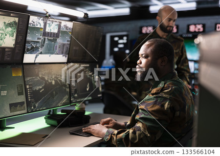 Soldiers working in governmental facility operating as military command post and surveillance monitoring center filled with digital equipment. Dispatchers doing job in base of operations 133566104