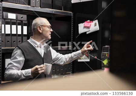 Senior criminologist studies fingerprints and records on a mystery board, using archived case files to uncover new clues in organized crime investigation. Gathering intelligence for a mission. 133566130