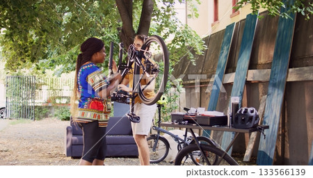 Athletic caucasian man safely dismantling damaged wheel from bicycle and helping young black woman with further maintenance. Active multiracial couple meticulously repairing bike components. 133566139