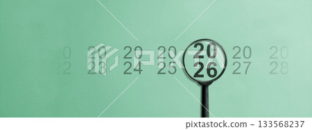Magnifying glass looking at the 2026 number on a colored background. Happy New Year concept or Celebration 133568237