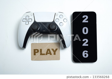 Modern white and black wireless gaming controller with a greeting card of Play and 2026 on a cellphone screen. Mockup or Copy space. Happy New Year concept or Celebration Modern white and black wireless gaming controller with a greeting card of Play and 2026 on a cellphone screen. Mockup or Copy space. Happy New Year concept or Celebration 133568268
