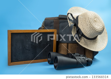 Chalkboard and Canvas bag with binoculars and a straw hat with a black ribbon on a blue background. Mockup or Copy space. Concept of travel, summer, or vacation Chalkboard and Canvas bag with binoculars and a straw hat with a black ribbon on a blue background. Mockup or Copy space. Concept of travel, summer, or vacation 133568314