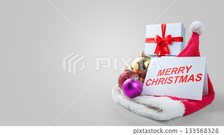 Greeting card of Merry Christmas with Christmas ornaments and a gift box with a Santa hat on a white background. Holiday greetings or winter themes. Concept of the Merry Christmas celebration 133568328