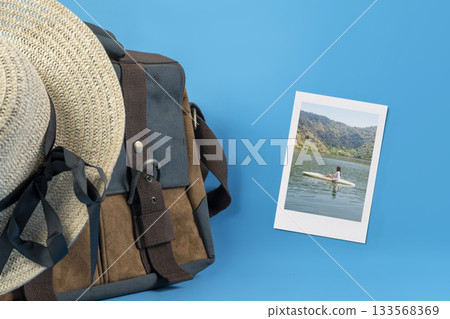 Instant print of an Indonesian southeast asian female paddling a kayak on a calm lake water and a canvas bag with a straw hat on a blue background. Mockup or Copy space. Concept of travel Instant print of an Indonesian southeast asian female paddling a kayak on a calm lake water and a canvas bag with a straw hat on a blue background. Mockup or Copy space. Concept of travel 133568369