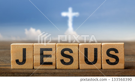 Row of wooden cubes with text of Jesus on the table with a cloud of Christian cross on a blue sky background. Concept of Christianity, religious, faith, Jesus, or belief 133568390