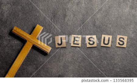 Christian cross and wooden cubes with Jesus text on a black background. Concept of Christianity, religious, faith, Jesus, or belief 133568395