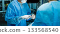 A surgeon wearing sterile gloves holds a large syringe containing medication. 133568540