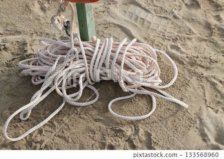White rope lying on the sand near a pole on the beach 133568960