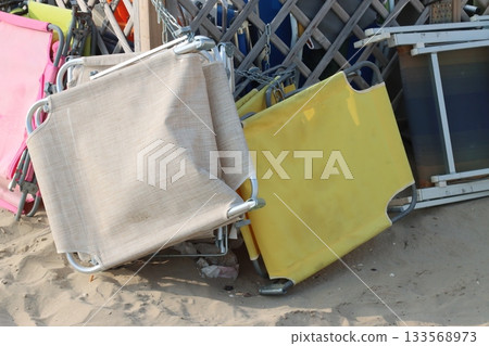 Stack of beach chairs laying on sand near wooden fence Stack of beach chairs laying on sand near wooden fence 133568973