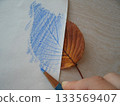 用藍色鉛筆在放在櫻花葉子上的紙片上描繪圖案。 133569407