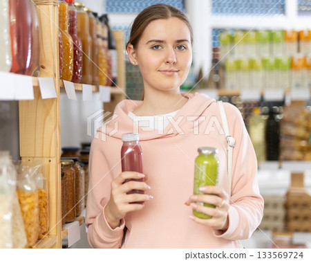 Girl customer in supermarket examines smoothie, chooses food-stuff in health lifestyle store Girl customer in supermarket examines smoothie, chooses food-stuff in health lifestyle store 133569724