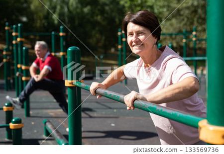 Mature woman doing push-ups from the crossbar on outdoor sports ground Mature woman doing push-ups from the crossbar on outdoor sports ground 133569736