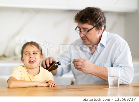 Father gives medicine to daughter to drink Father gives medicine to daughter to drink 133569737
