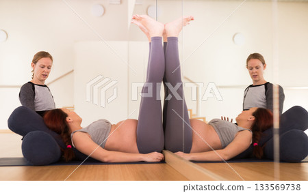 Pregnant woman practices yoga with an instructor. Bent Candle Pose or Viparita Karani Pregnant woman practices yoga with an instructor. Bent Candle Pose or Viparita Karani 133569738
