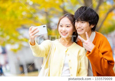 A couple taking a selfie in front of a ginkgo tree A couple taking a selfie in front of a ginkgo tree 133570009