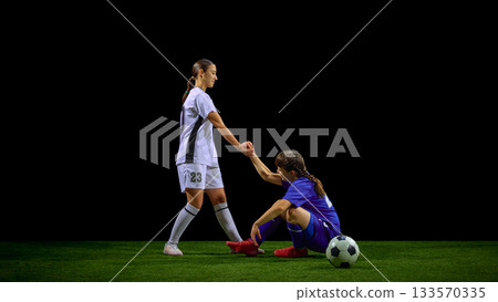 Teenage girls soccer player helping teammate rise after fall during match 133570335