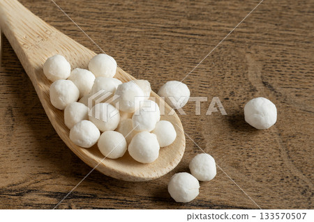 White dry tapioca pearls in wooden scoop on wooden background closeup. Raw tapioca starch balls used for bubble tea or desserts. Tapioca pearls as healthy gluten free ingredient. 133570507