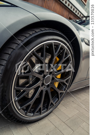 Close-up view of sleek car wheel with striking design and details in urban setting Close-up view of sleek car wheel with striking design and details in urban setting 133570816