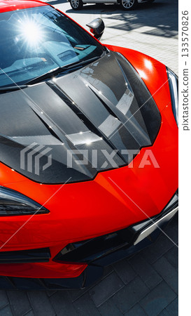 Stunning red sports car with carbon fiber hood parked in bright sunlight 133570826