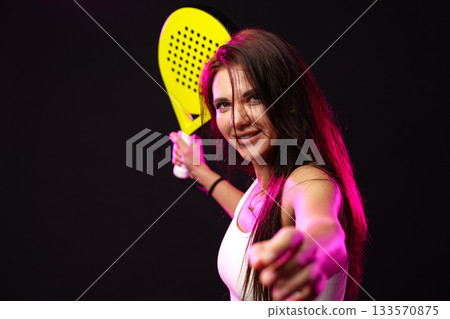 Woman holds a bright paddle and poses confidently against a dark background Woman holds a bright paddle and poses confidently against a dark background 133570875