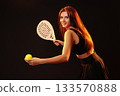 Woman preparing to serve in a racket sport with a bright smile and a tennis ball 133570888