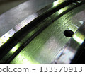 Extreme close-up of a metallic surface, possibly a bearing or machine part, showing wear, fine grooves, and visible cracks under bright, greenish light. Generator seal. 133570913