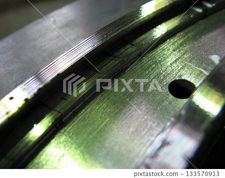 Extreme close-up of a metallic surface, possibly a bearing or machine part, showing wear, fine grooves, and visible cracks under bright, greenish light. Generator seal. 133570913