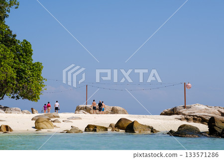 Tourists stroll along the tropical beach of Lang Tengah Island, enjoying the coastline and clear blue sky. Malaysia 133571286