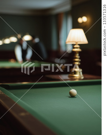 Cue ball on green billiard table felt, showing a vintage game setting in a dimly lit club with people playing pool in the background, leisure and recreation indoors 133571316