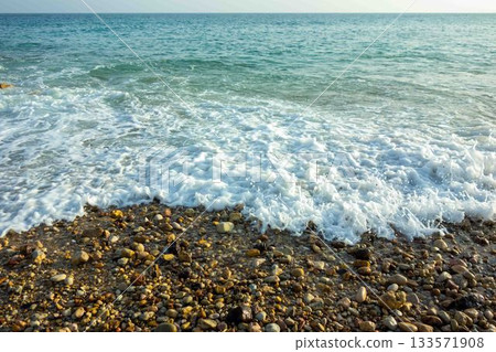Ocean waves breaking on a beautiful pebble beach white foam bubbles turquoise water Ocean waves breaking on a beautiful pebble beach white foam bubbles turquoise water 133571908