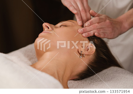 Relaxation during a soothing head massage in a calm spa setting with a focused therapist and a tranquil client experiencing blissful rejuvenation 133571954