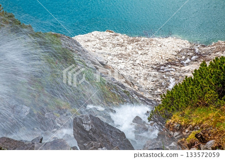Steep mountain waterfall plunging toward turquoise alpine lake 133572059