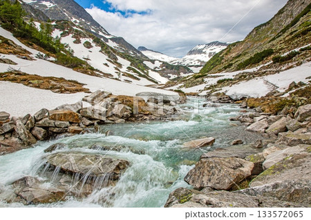 Alpine river flowing through snowy valley with rocky banks 133572065
