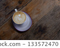 Delicious latte with heart-shaped latte art on a wooden table in a coffee shop atmosphere. 133572470