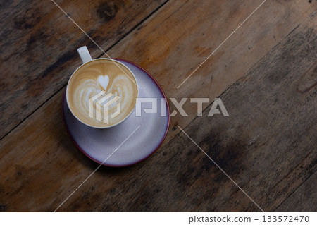 Delicious latte with heart-shaped latte art on a wooden table in a coffee shop atmosphere. 133572470