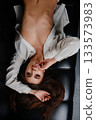 Attractive woman in oversized shirt lying upside down on a black sofa 133573983