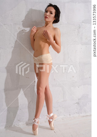Ballet dancer posing gracefully against a white wall in a studio setting Ballet dancer posing gracefully against a white wall in a studio setting 133573996