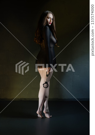 Elegant woman in sheer dress holding handcuffs in a dramatic indoor setting at night Elegant woman in sheer dress holding handcuffs in a dramatic indoor setting at night 133574000