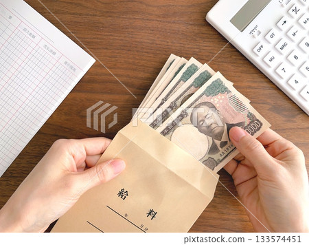 A woman's hand taking out banknotes from a pay envelope on a desk 133574451