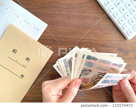 Woman's hands counting pay envelope and banknotes on desk Woman's hands counting pay envelope and banknotes on desk 133574453