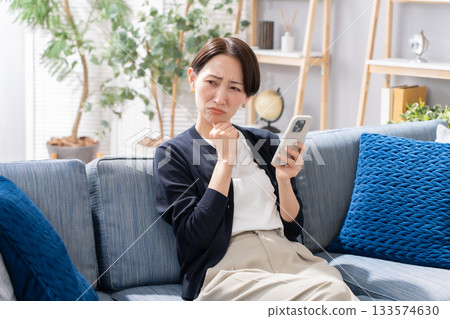A woman operating a smartphone on the sofa is worried A woman operating a smartphone on the sofa is worried 133574630