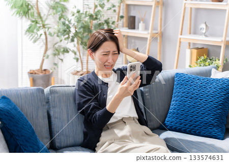 一位坐在沙發上操作智慧型手機的女士感到擔憂。 一位坐在沙發上操作智慧型手機的女士感到擔憂。 133574631