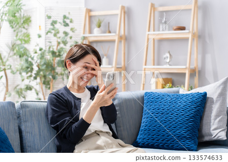 A woman operating a smartphone on the sofa is worried A woman operating a smartphone on the sofa is worried 133574633
