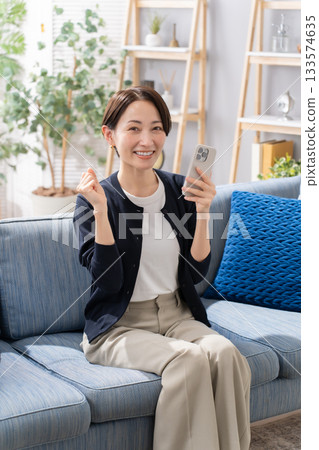 A woman operating a smartphone on the sofa, fist pump A woman operating a smartphone on the sofa, fist pump 133574635