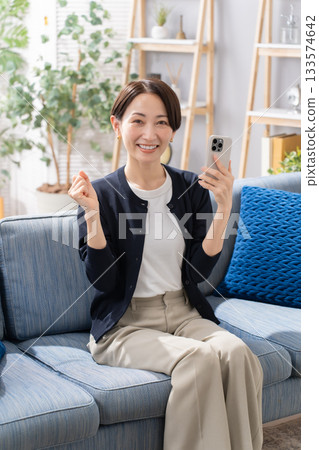 一名女子在沙發上操作智慧型手機，握拳慶祝 133574642