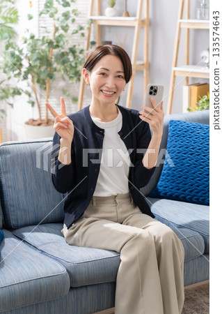 A woman operating a smartphone on the sofa Peace sign 133574643