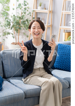 A woman operating a smartphone on the sofa Peace sign 133574644