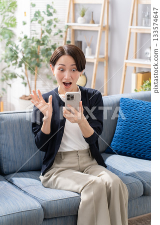 A woman operating a smartphone on the sofa is surprised A woman operating a smartphone on the sofa is surprised 133574647