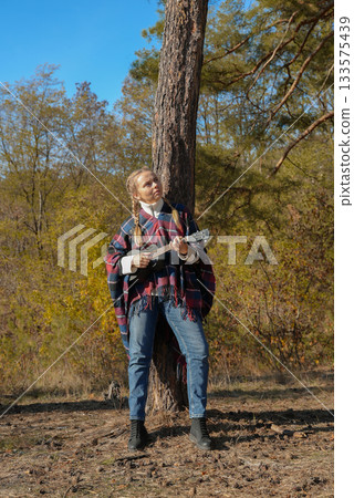 Beautiful blonde girl playing guitar ukulele and singing relaxing enjoying outdoors on sunny autumn day. Hippie woman in boho style training playing musical instrument. Fall leaves 133575439