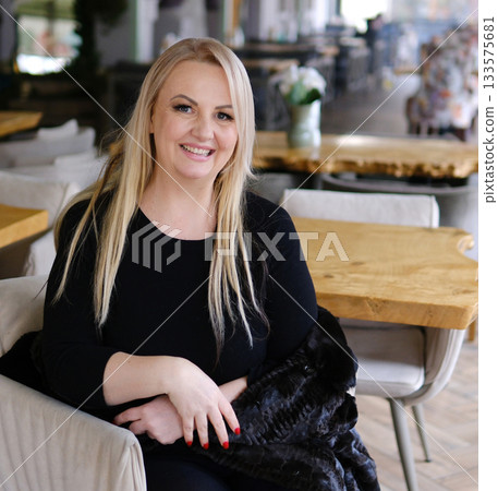 Beautiful mature lady resting on home sofa, looking at camera wit serious face, getting positive, happy, smiling, leaning head, touching nap. Pretty middle aged woman portrait 133575681